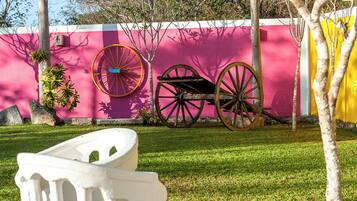 A white outdoor sculpture, a pink wall, and a tree in a grassy area.