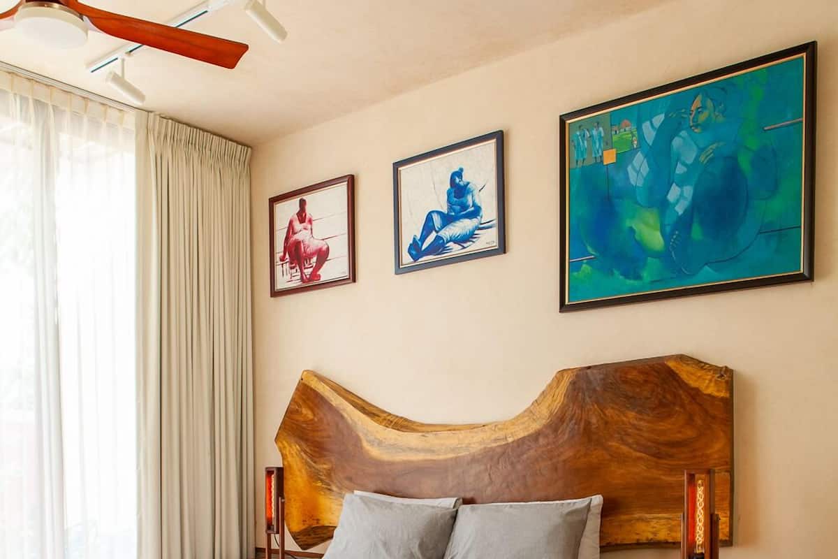 A bedroom with a wooden headboard, a bed with grey bedding, a small wooden table, and artwork on the walls.