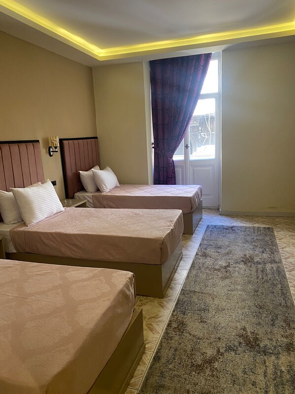 A hotel room with two beds, a large window with purple curtains, and a carpeted floor. - Golden Hoster (Alexandria)