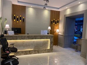 A reception area with a marble reception desk, two black chairs, wooden paneling, wall-mounted lights, and a view of a cityscape through a window. - Golden Hoster (Alexandria)