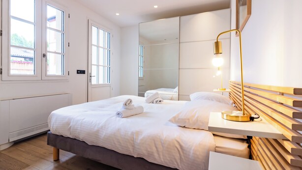 Un hotel moderno con una cama grande, una mesita de noche con lámpara, un espejo y vistas al exterior a través de las ventanas.