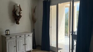 Une pièce avec un meuble blanc, un élément décoratif mural et une vue sur l’extérieur, visible à travers une porte vitrée.