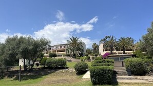 Un quartier résidentiel avec un immeuble doté de nombreux balcons, entouré de jardins bien entretenus et de palmiers.