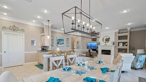 A dining area with a wooden table set for six, a chandelier, and a television in the background.