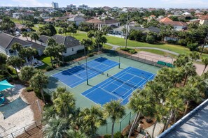 Un court de tennis entouré de maisons d’habitation et de palmiers.