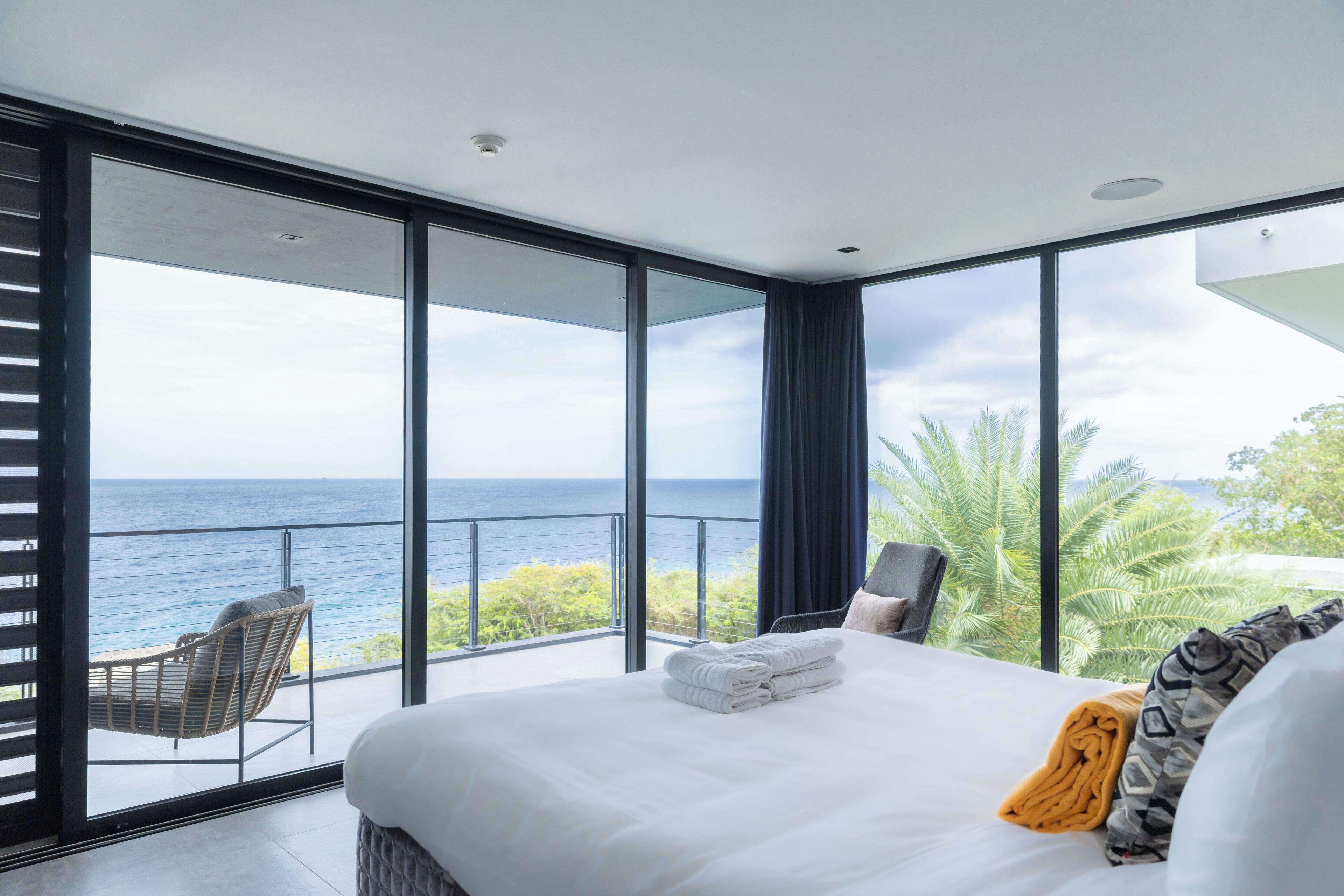 Una habitación de hotel moderna con una cama grande, vista al océano y un balcón con una silla.
