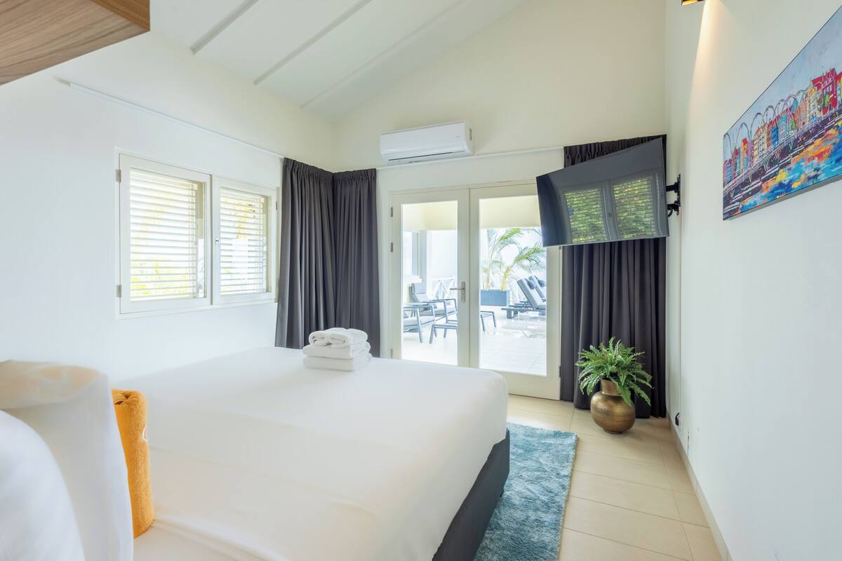 A hotel room with a large bed, a balcony with a table and chairs, and a potted plant.