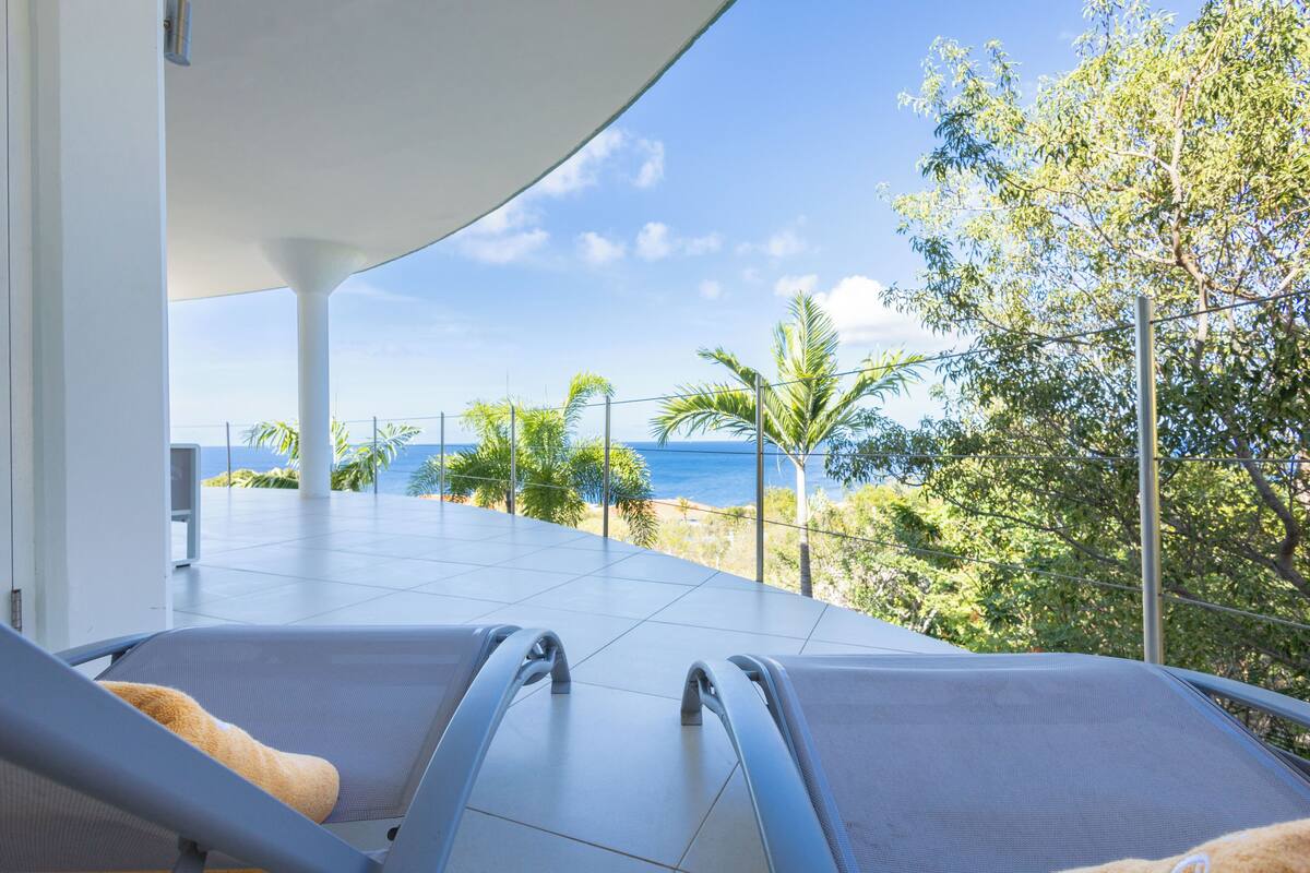A balcony with two lounge chairs and a view of the ocean.