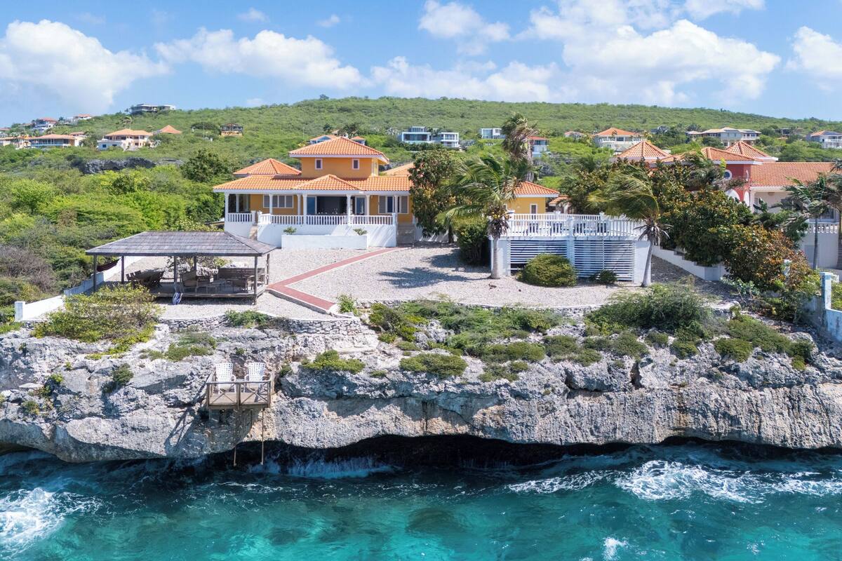 A coastal property with a rocky shoreline, a covered patio, and a view of the sea.