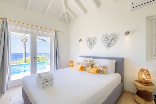 Un dormitorio con cama, mesita de noche, decoración en la pared y vista al océano a través de una puerta corrediza.