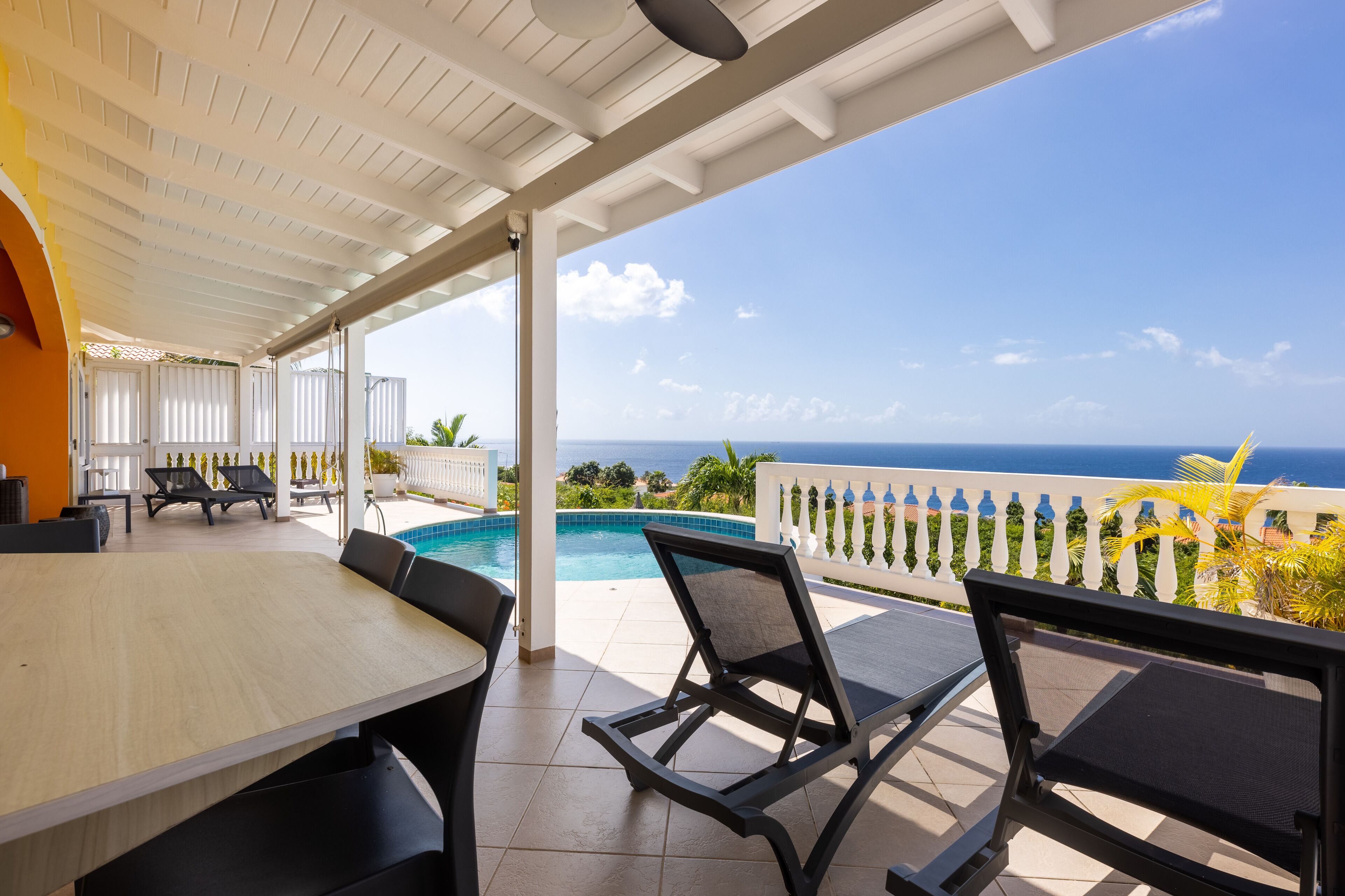 A covered outdoor area with a pool, lounge chairs, and a view of the ocean.