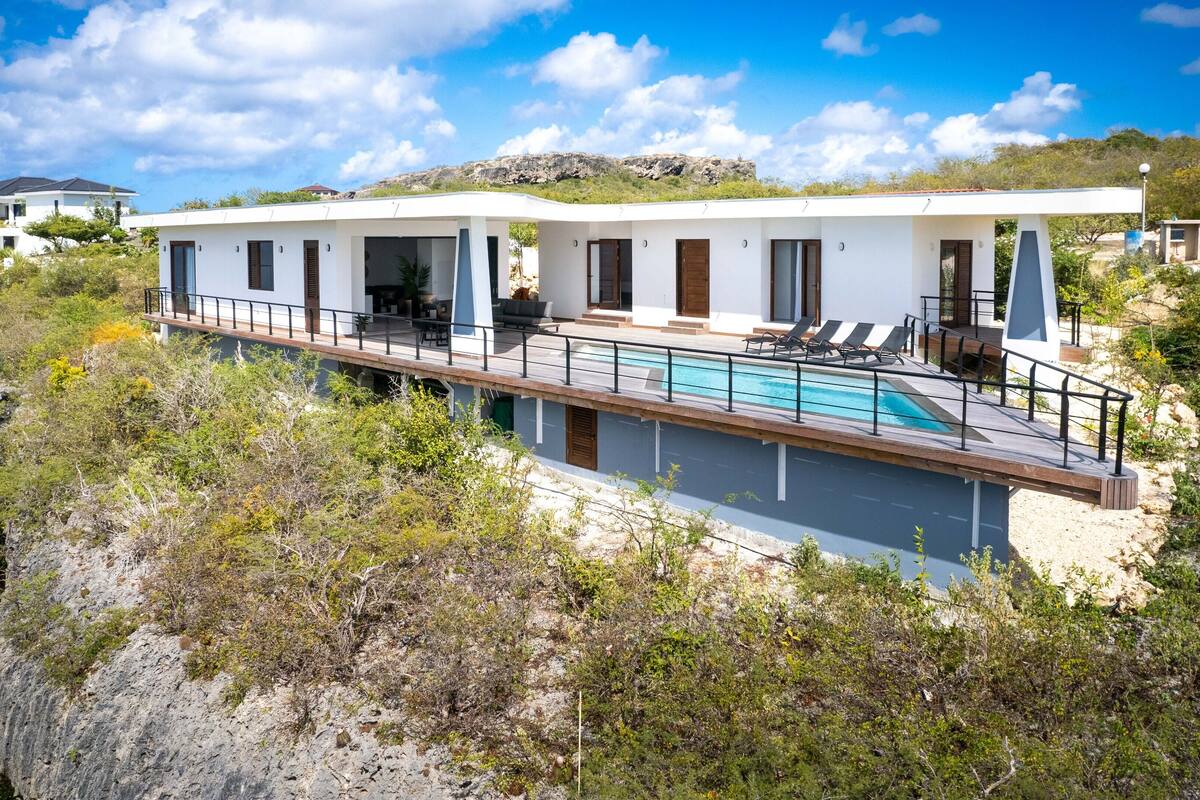 A modern villa with a pool, multiple rooms, and a view of the surrounding landscape.