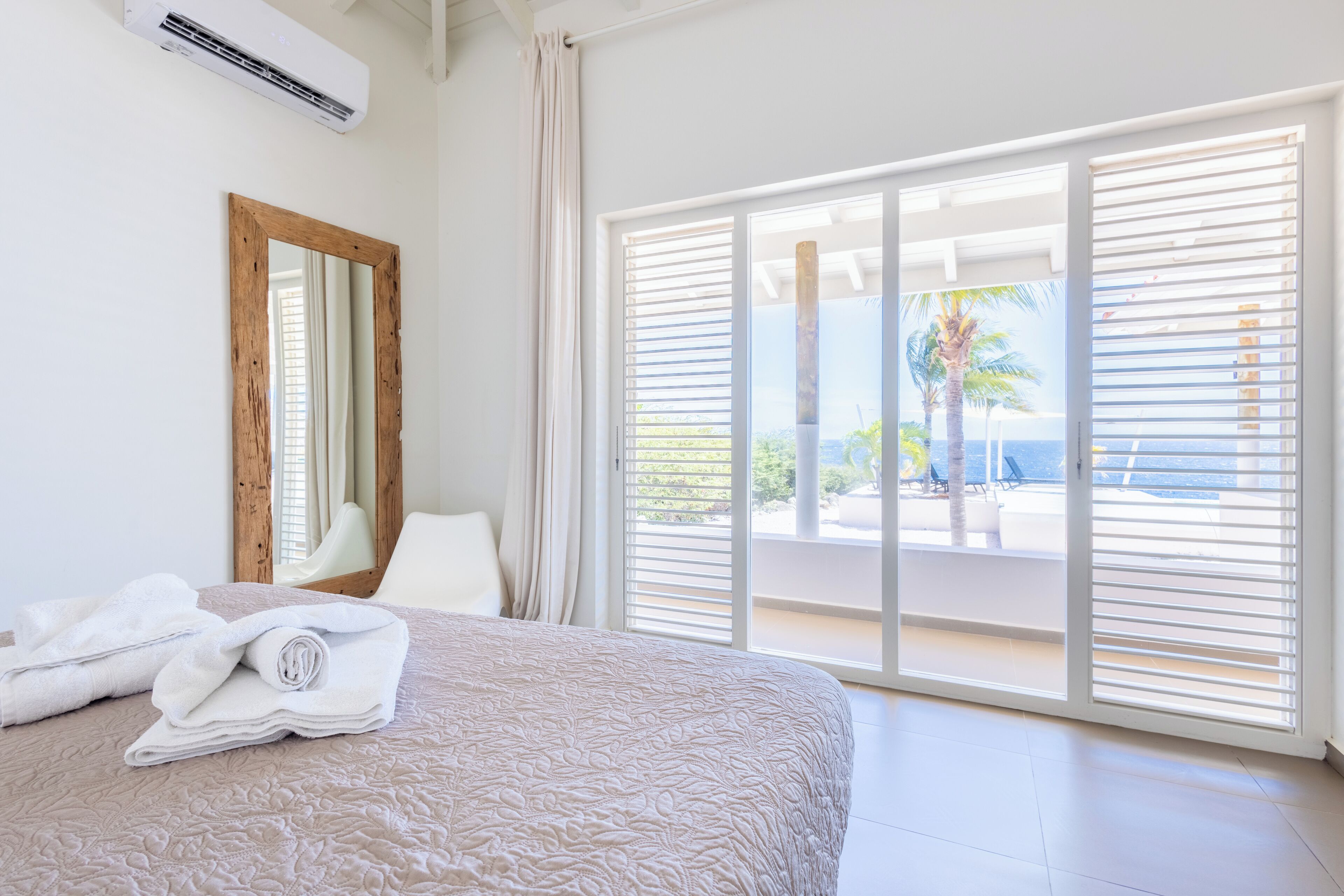 Une chambre d’hôtel avec un grand lit, un miroir, une fenêtre avec des stores et une vue sur l’extérieur.