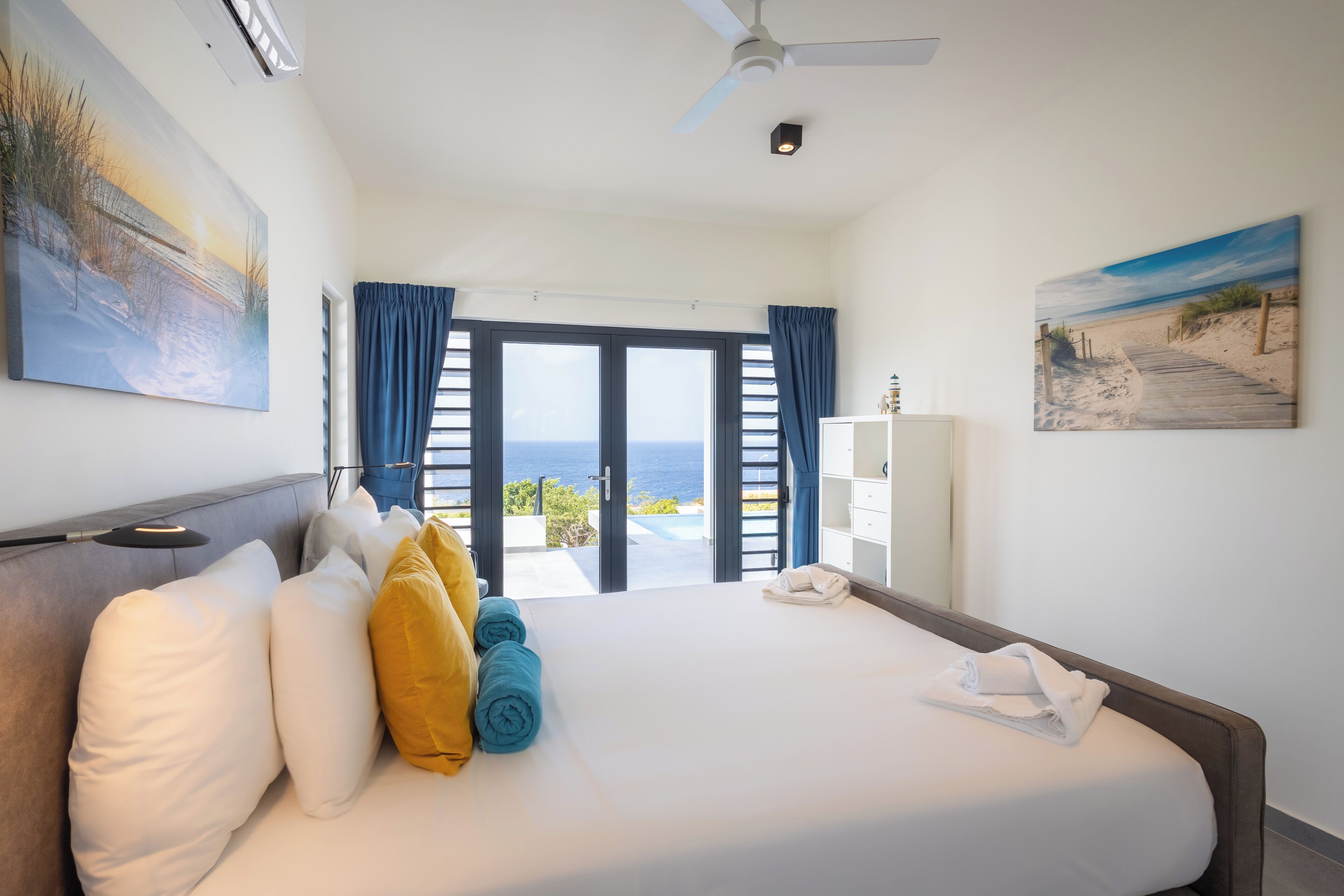 A hotel room with a large bed, a ceiling fan, and a view of the ocean through the open door.