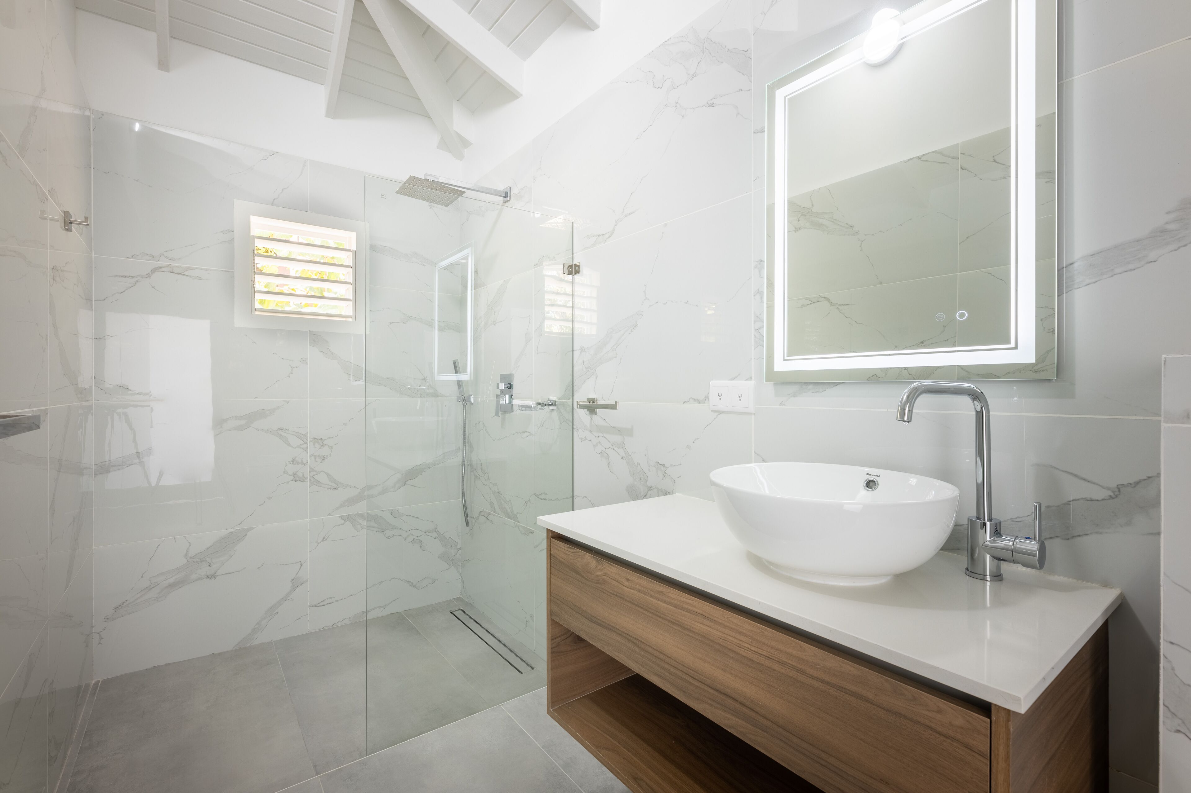 Een moderne badkamer met een douche in een glazen cabine, een witte wastafel en een houten opbergmeubel.