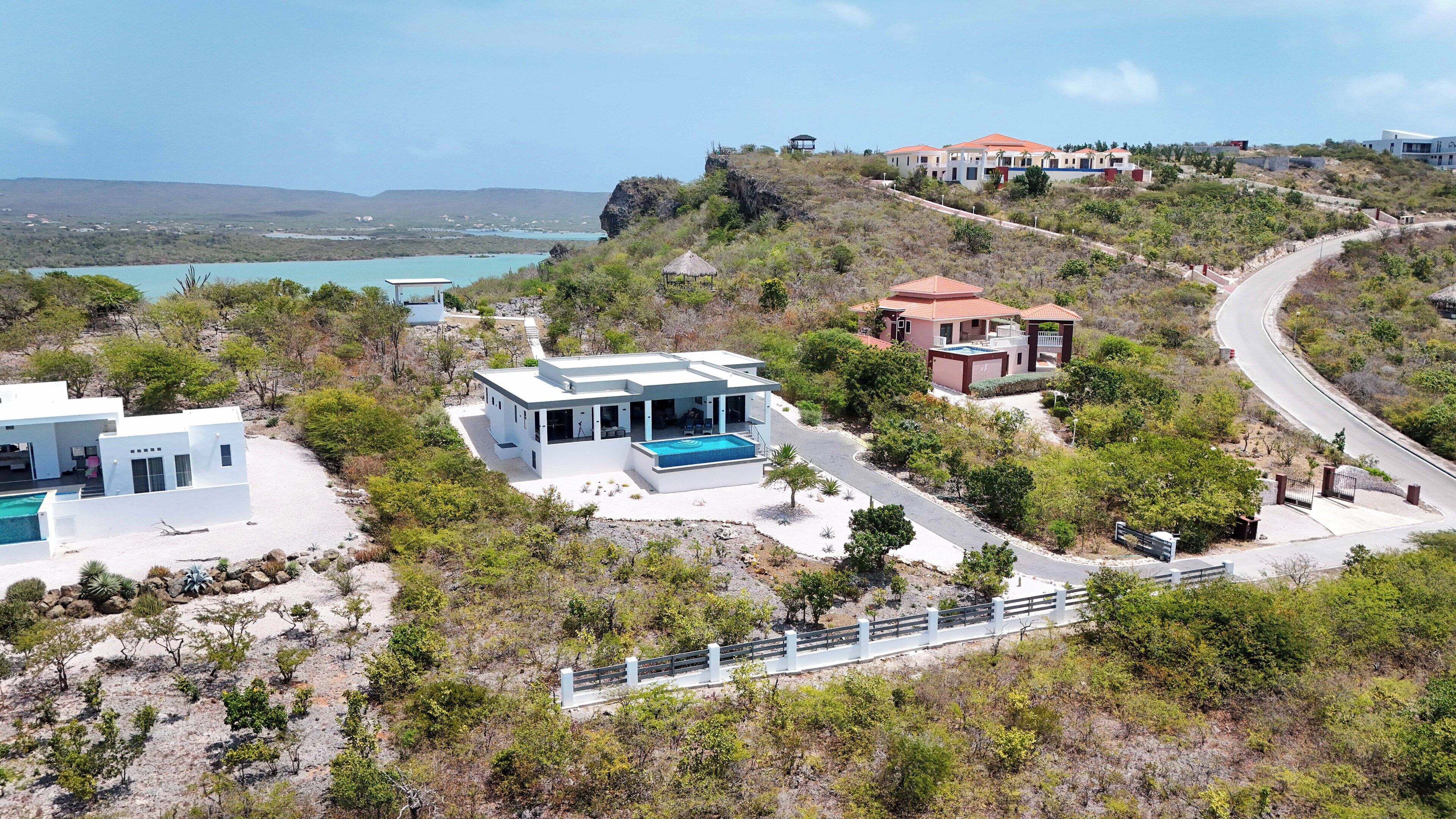 A modern villa with a swimming pool, surrounded by natural landscape and a view of the sea.