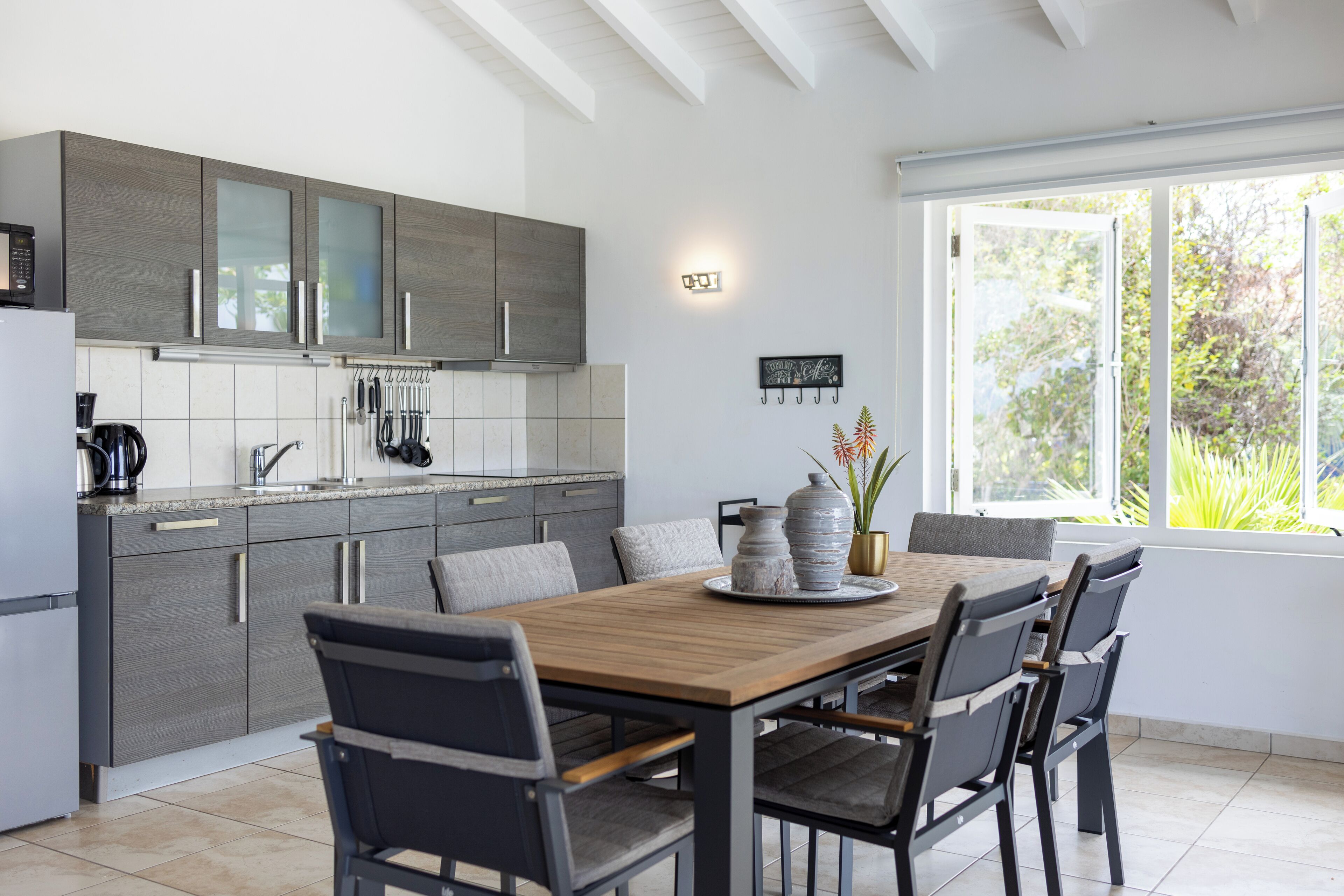 Une cuisine moderne avec des meubles gris, une table à manger en bois et une fenêtre donnant sur un paysage verdoyant.