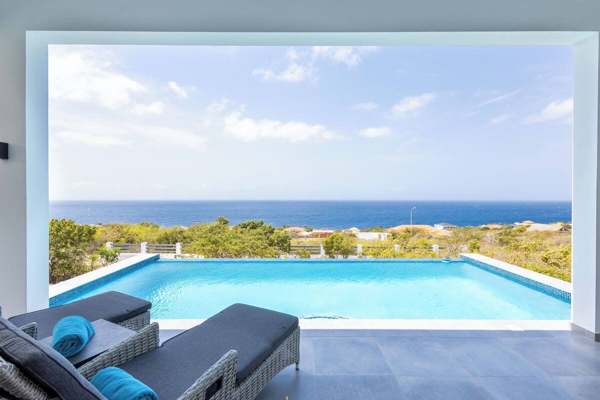 A poolside area with a view of the ocean, a lounge chair, and a small pool.
