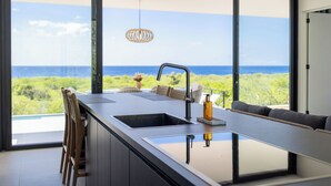 A modern kitchen with a large window overlooking a scenic view of the ocean and greenery. - Coral Estate Holidays (St. Marie)