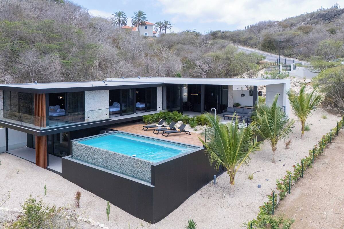 A modern two-story house with a swimming pool, outdoor seating, and a view of the surrounding landscape.