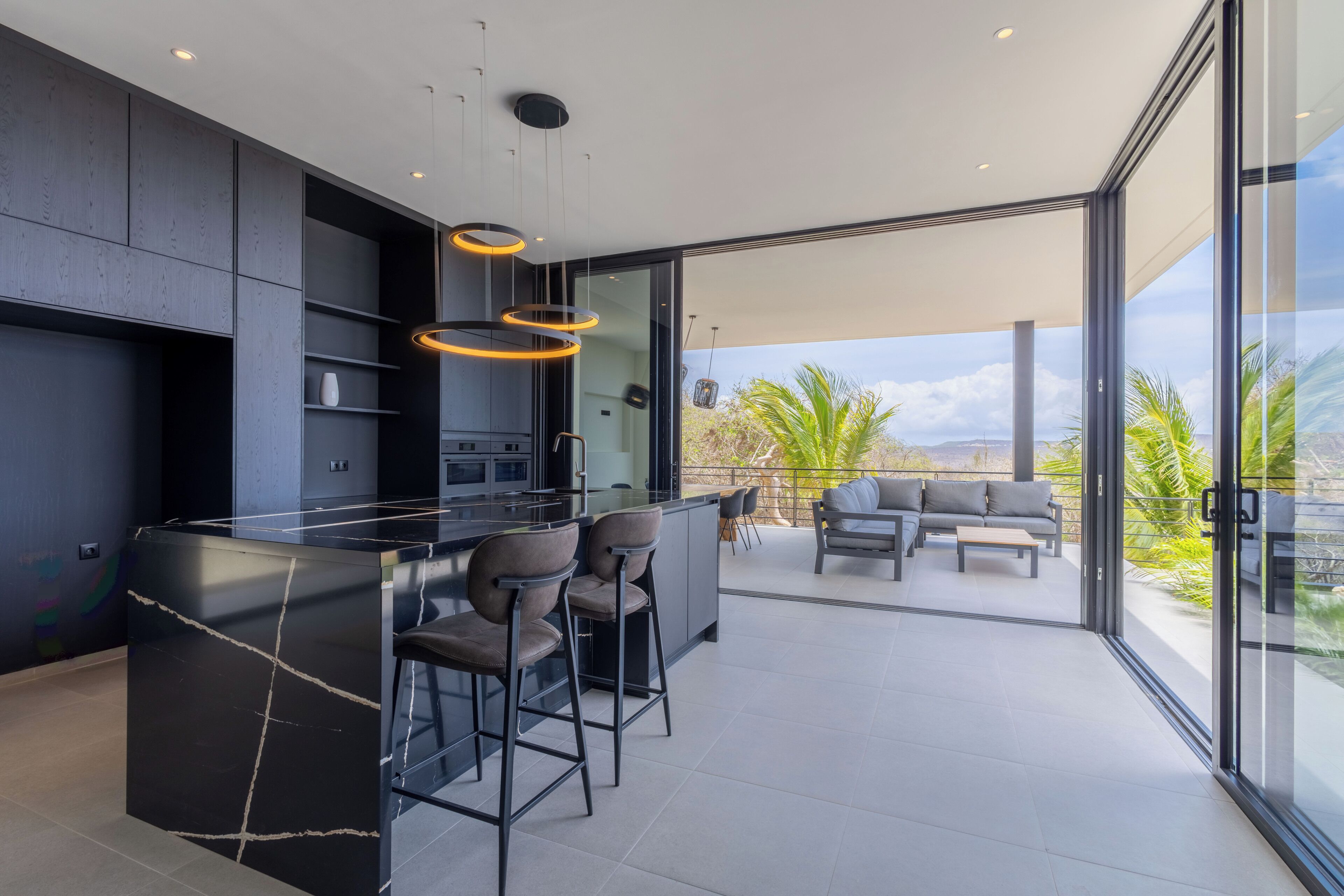 Eine moderne Küche mit Barbereich, großen Fenstern und einer Terrasse mit Außenmöbeln.