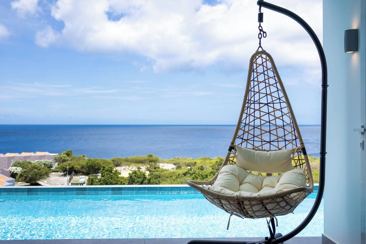 A hanging chair by a pool with a view of the ocean.