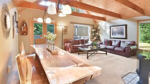 A spacious living area with a wooden ceiling, a large wooden dining table, a leather sofa, and a television.