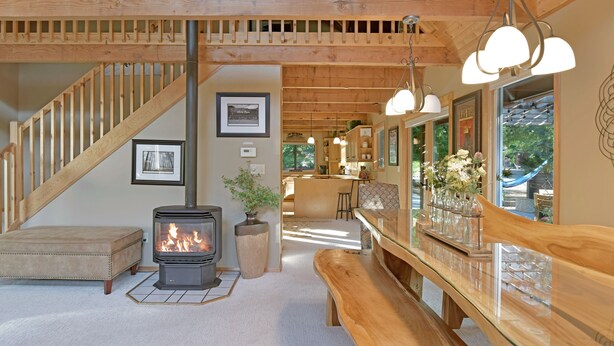 A cozy interior with a wooden staircase, a fireplace, a bench, and a dining area with a view of the outdoors.
