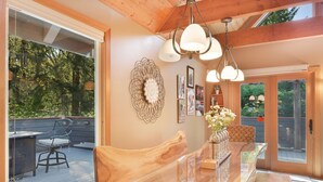 A wooden dining table with a glass top, surrounded by chairs, in a room with wooden beams and pendant lights.