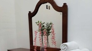 Un aparador de madera con espejo, un jarrón con flores rosadas y toallas blancas enrolladas.