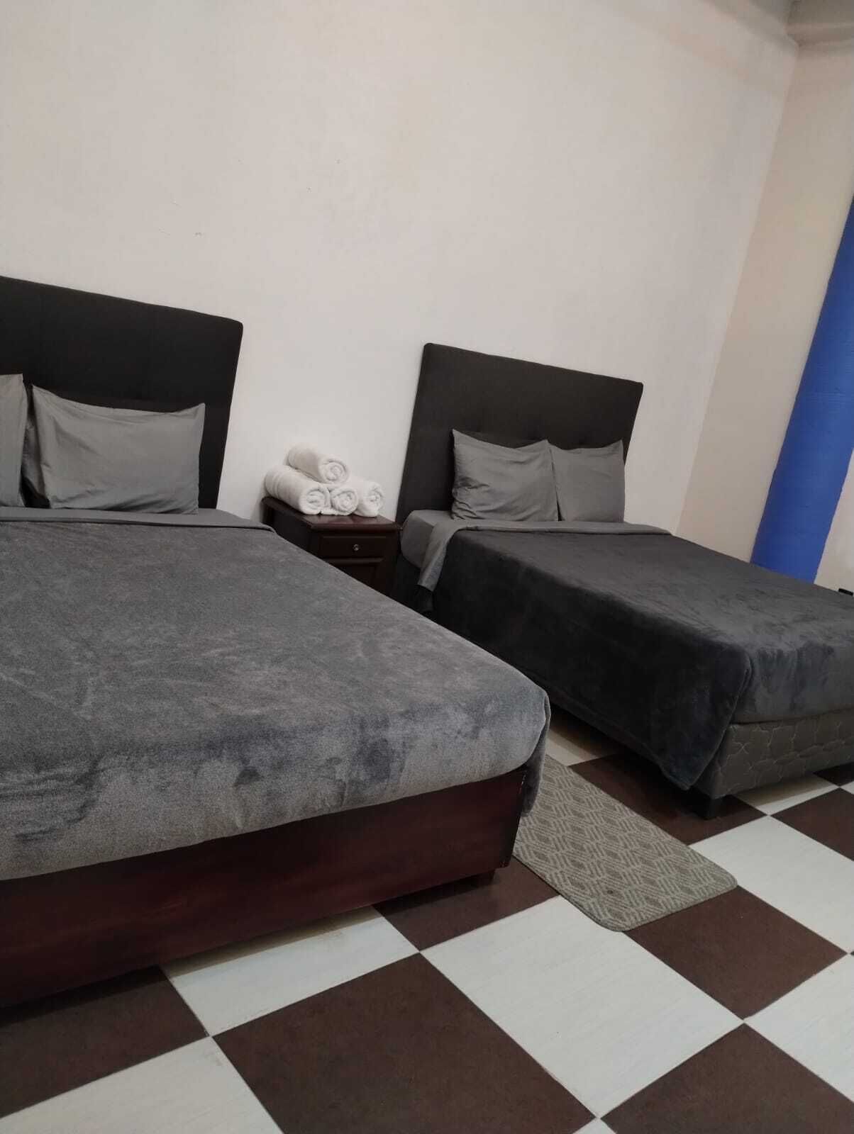 A room with two beds, a small bedside table with a lamp, and a checkered floor.