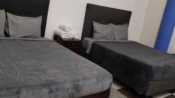 A room with two beds, a small bedside table with a lamp, and a checkered floor.