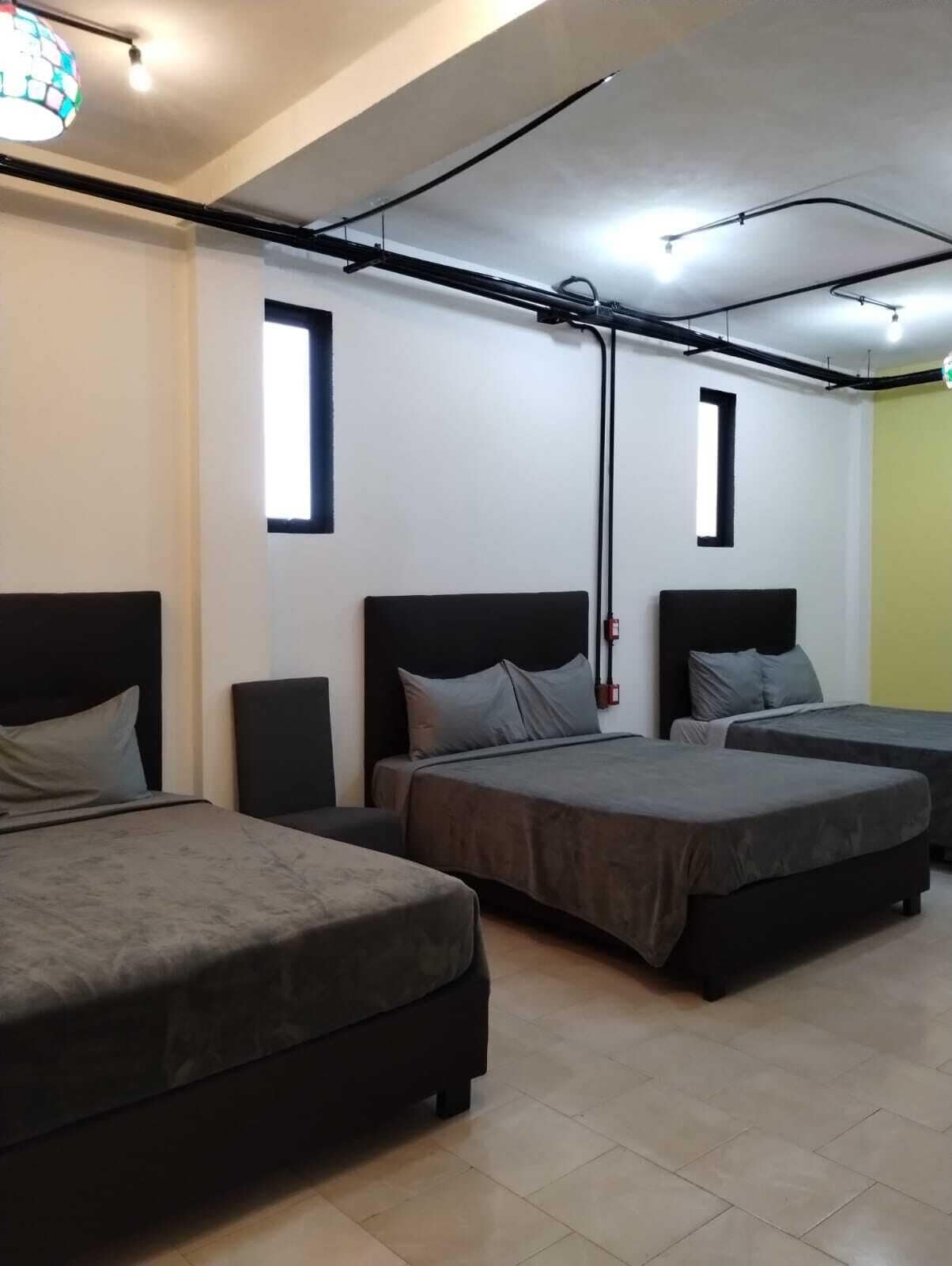 A hotel room with three beds, a window, and a ceiling light fixture.