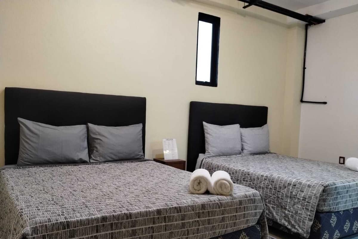 Two beds with headboards, a small window, and a wall-mounted light fixture.