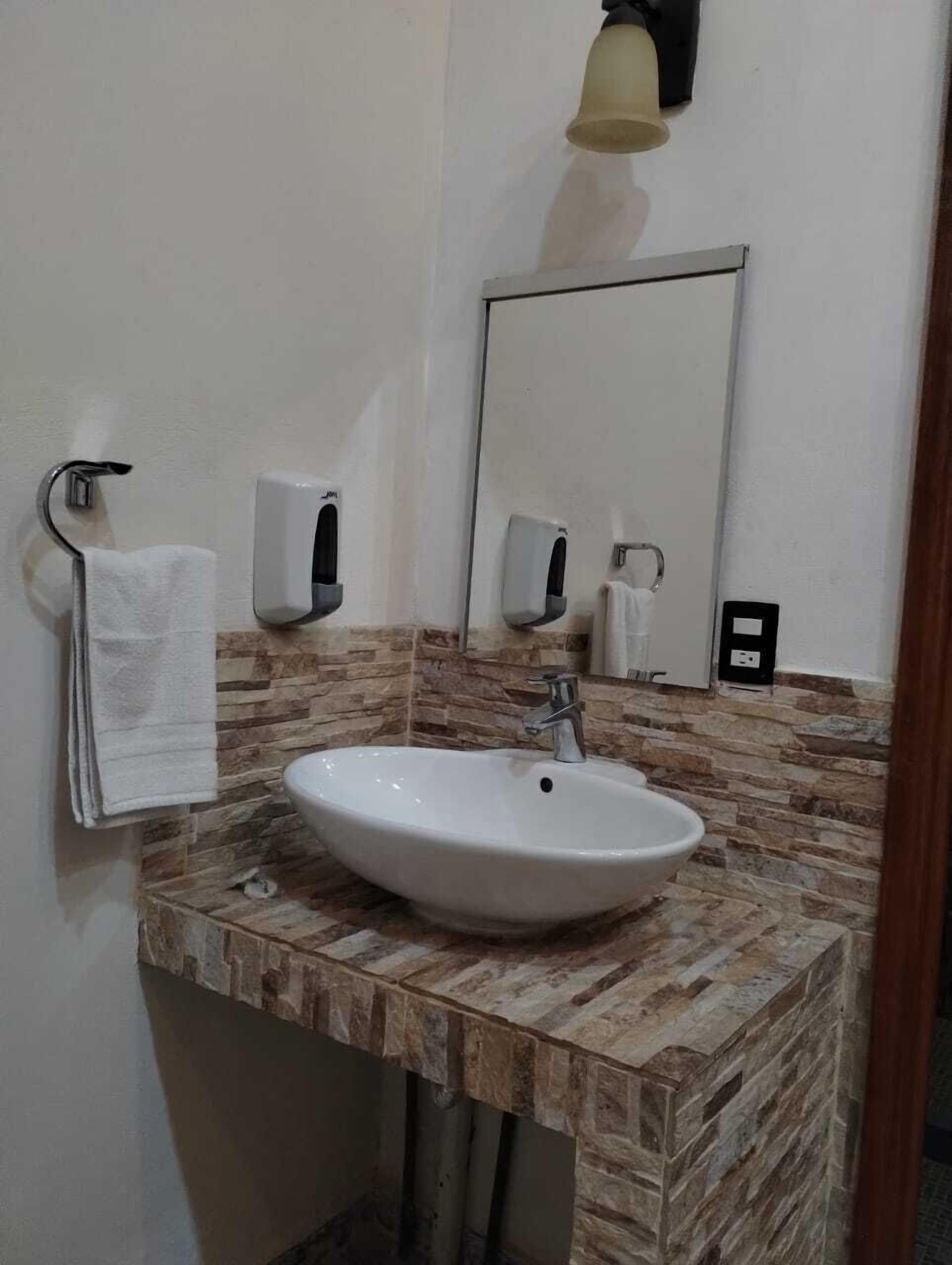 A bathroom with a white sink, a mirror, a towel rack, and a soap dispenser.