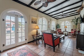 A spacious living area with a high ceiling, large windows, and a view of the outside. There are several pieces of furniture, including a sofa, chairs, and a table.