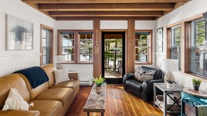 A cozy living room with a wooden ceiling, two sofas, a coffee table, and a view through a door to an outdoor area. - Ocean Views from 2 Decks! Beachfront ⎮ Amphitrite (Ucluelet)