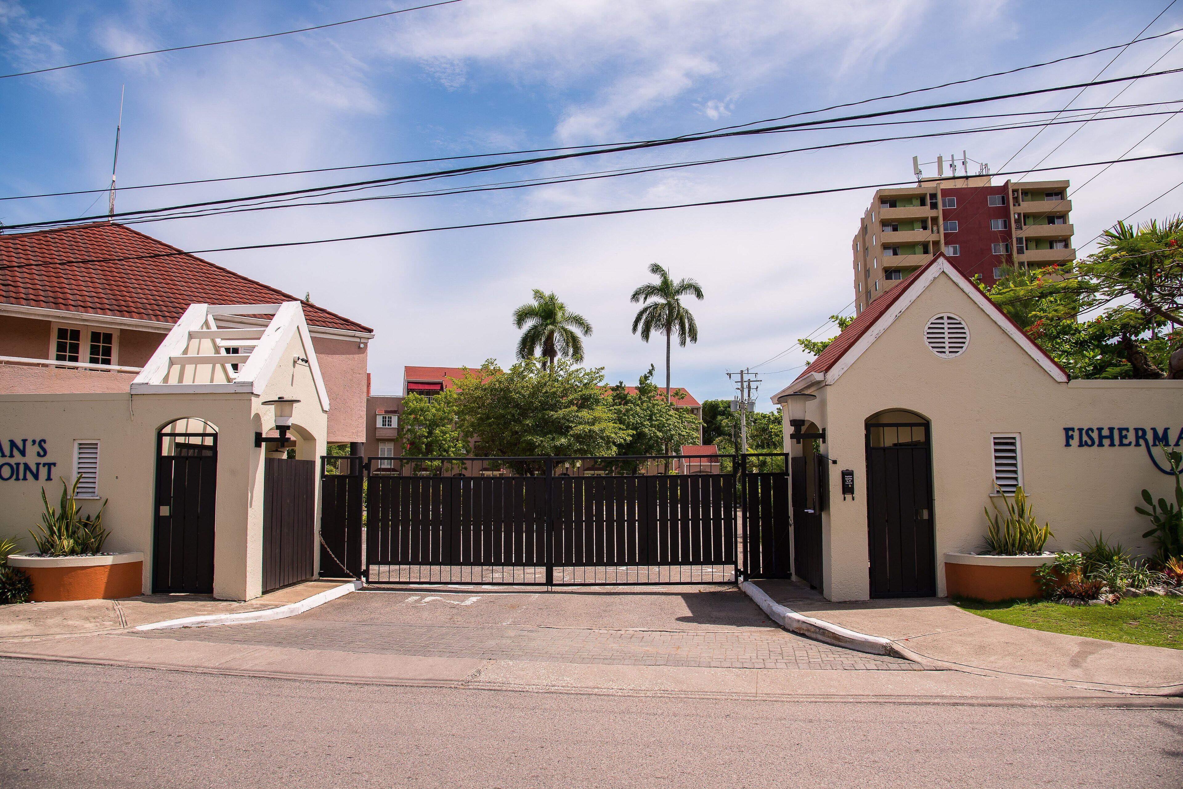 A gated entrance with a black gate, a building labeled "FISHERMAN'S POINT," and a palm tree in the background.