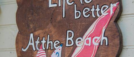 Un letrero de madera con el texto 'Life is better at the beach' e ilustración de un velero.
