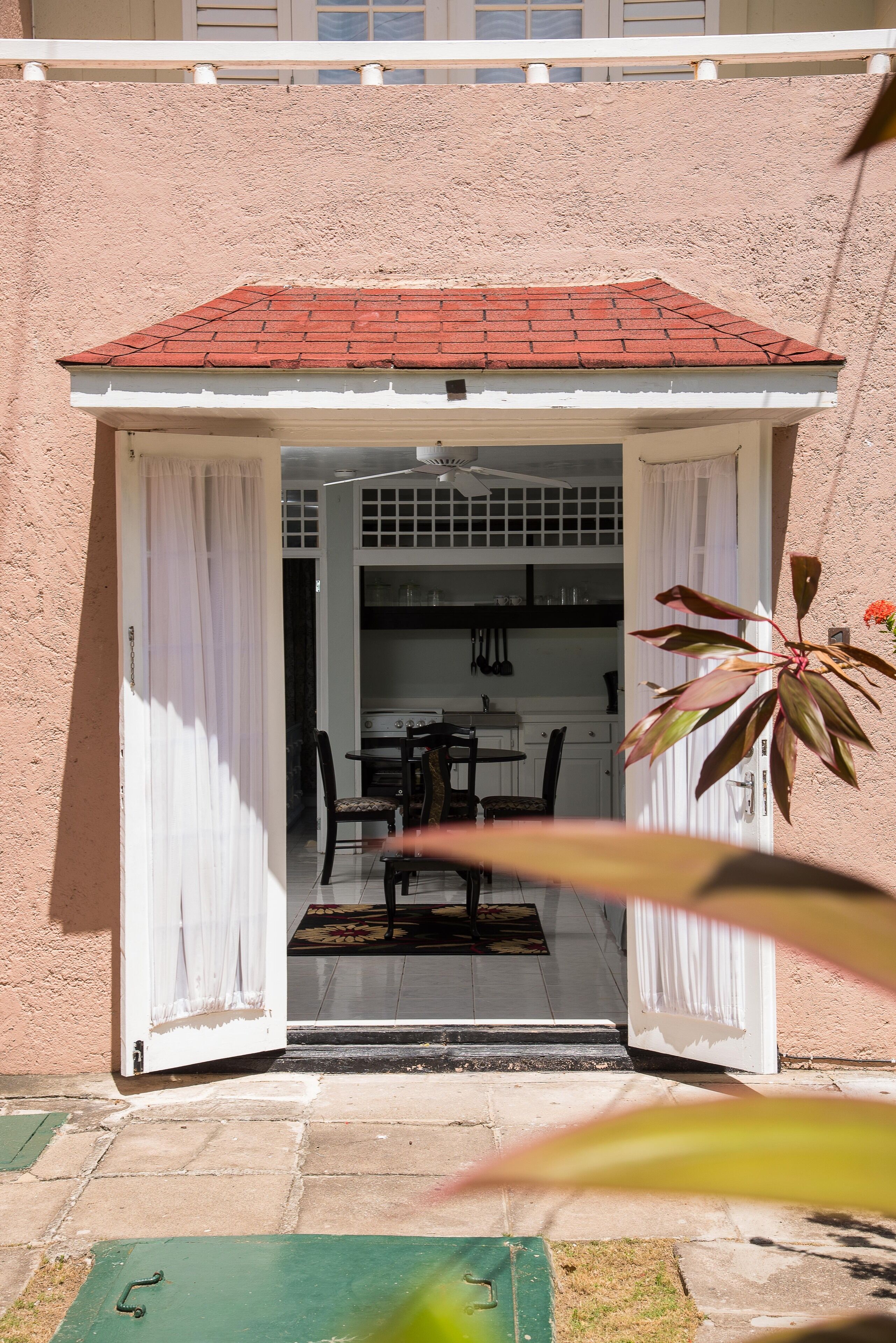 A building entrance with a red-tiled roof, white exterior walls, and a covered patio area with a table and chairs.