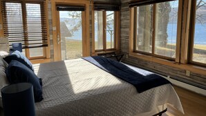 A bedroom with a large bed, wooden walls, and a view of a lake. - Moonlight Manor on Keuka Lake in Hammondsport (Hammondsport)