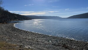A lakeside view with a pebbly shore, distant hills, and a clear sky. - Moonlight Manor on Keuka Lake in Hammondsport (Hammondsport)