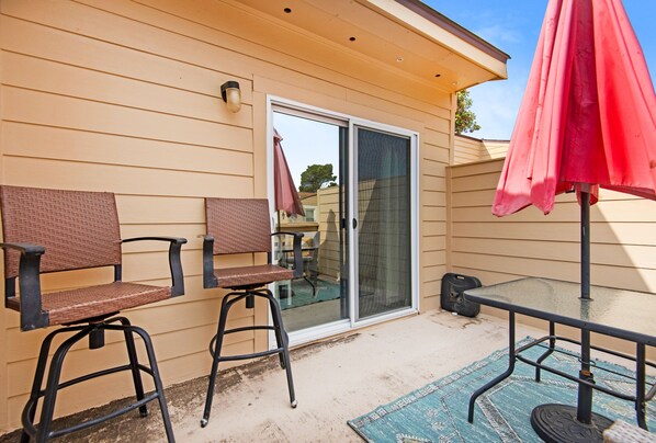 An outdoor patio with two wicker chairs, a glass table, and a red umbrella.