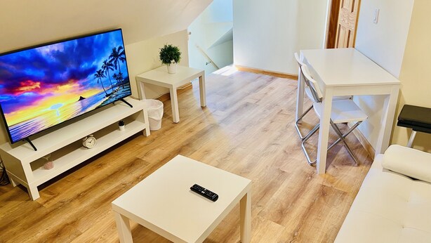 A modern living room with a flat-screen TV, white furniture, and a wooden floor. - Bright, Stylish & Cozy Private Attic Unit near NYC (HALEDON)