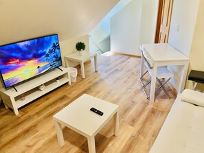 Una sala de estar moderna con un televisor de pantalla plana, muebles blancos y piso de madera.