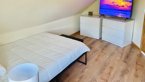 A bedroom with a bed, a TV on a dresser, and a view of the sky. - Bright, Stylish & Cozy Private Attic Unit near NYC (HALEDON)