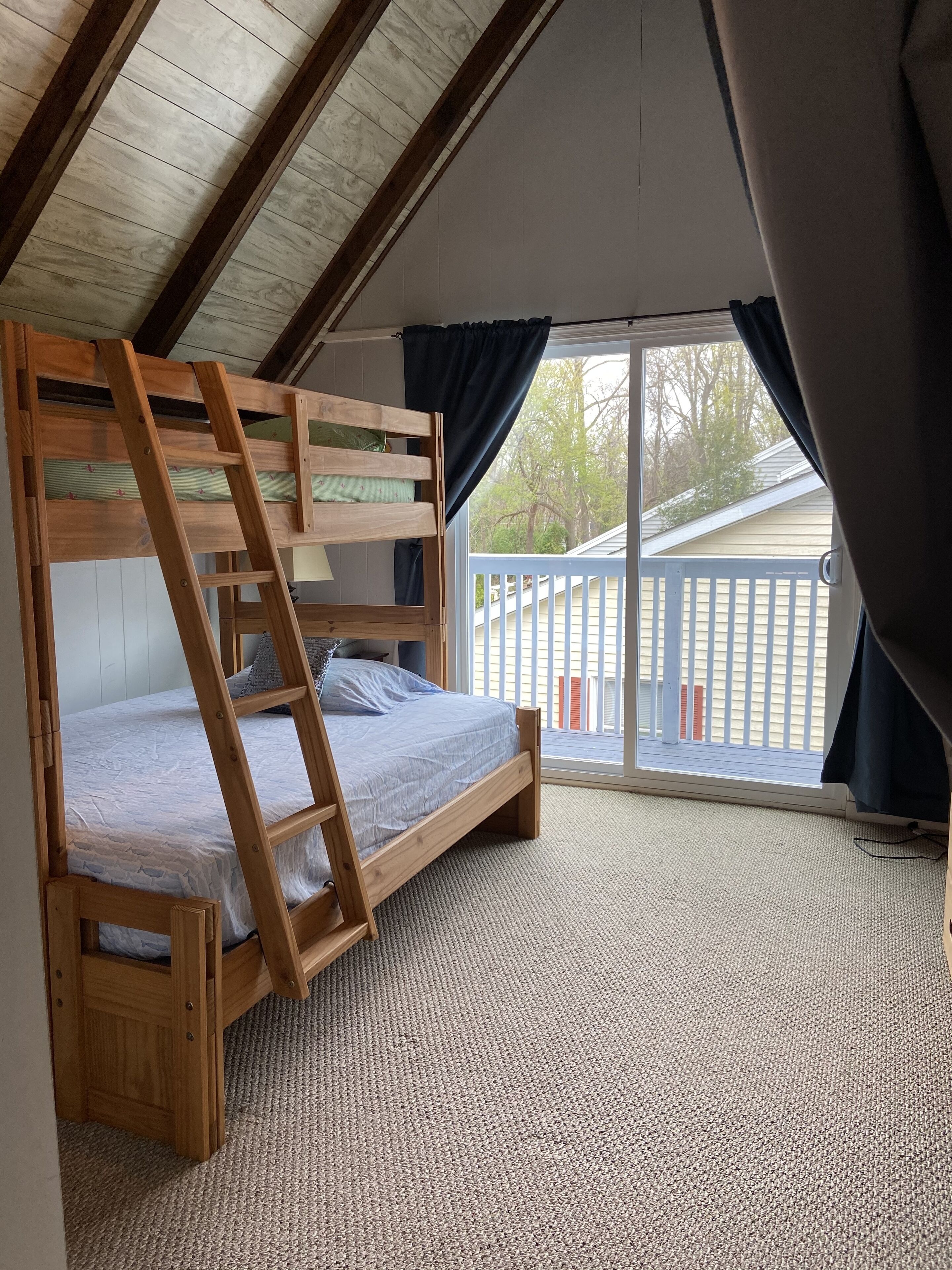 Un lit superposé avec une échelle en bois, un sol recouvert d’une moquette et une vue sur un balcon doté d’une balustrade.