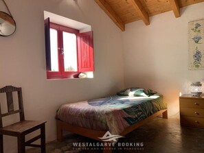 Cozy bedroom with a comfortable bed, wooden chair, and nightstand, featuring a window with shutters.