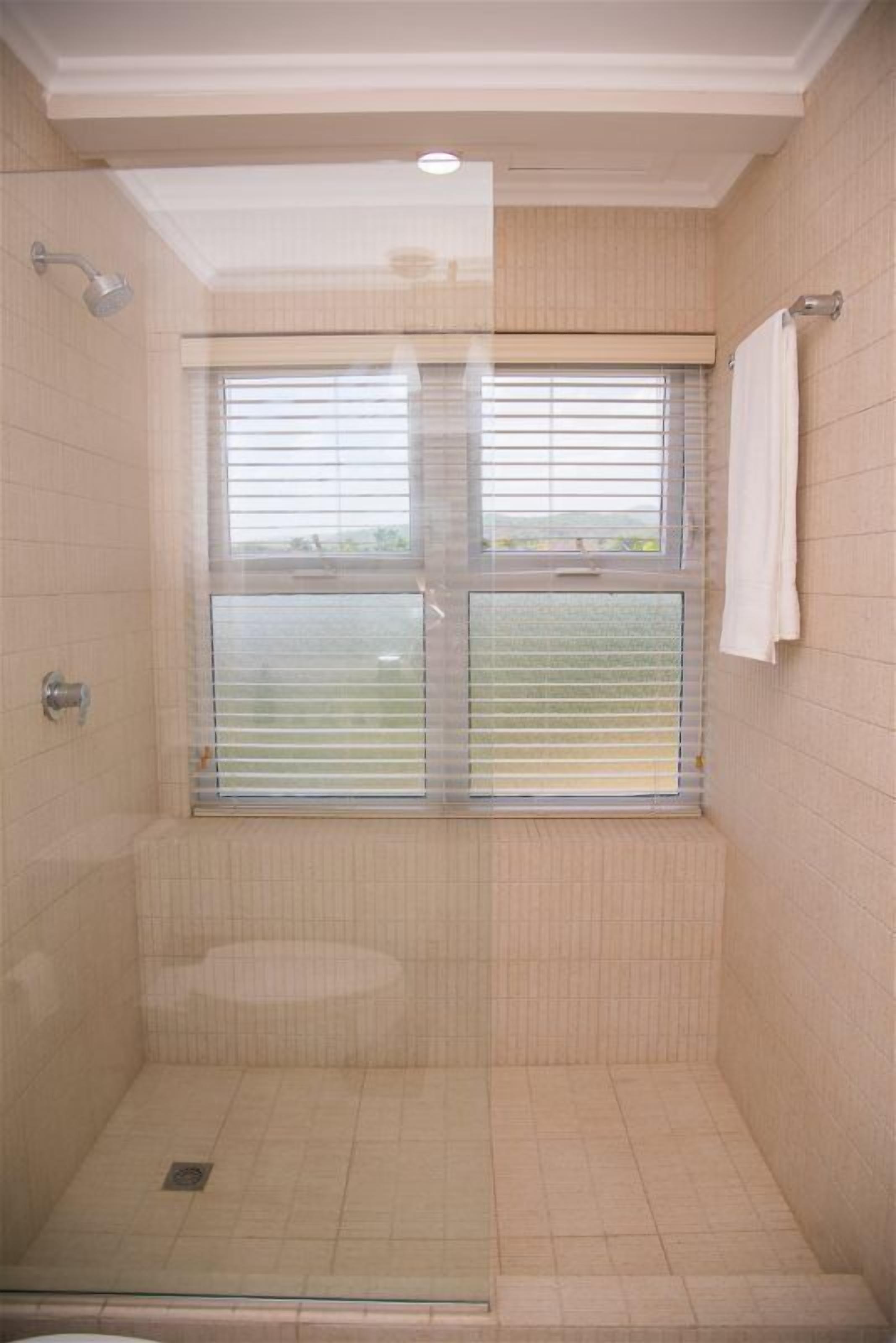 A shower with a window, tiled walls, and a towel hanging on the wall.