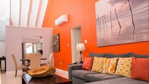 A living room with a grey sofa, orange walls, and a painting of trees. - Imperial Topaz At Richmond (St. Ann's Bay)